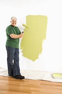 Middle-aged man painting wall green with paint roller smiling at viewer.