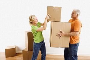 Man holding cardboard moving boxes while woman places one on stack