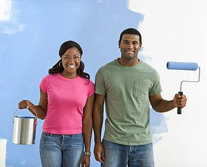 Couple next to half-painted wall with paint supplies