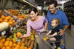 Parents grocery shopping for fruit with toddler