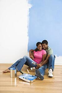 Couple sitting together relaxing next to half-painted wall and painting supplies