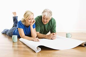 Couple laying on floor looking at architectural blueprints together
