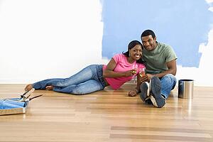 Couple relaxing together with wine next to half-painted wall and painting supplies
