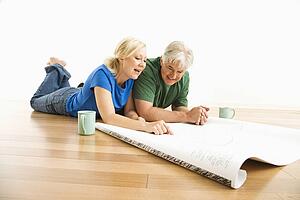 Middle-aged couple lying on floor looking at and discussing architectural blueprints together.