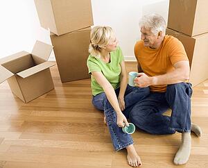 Couple sitting on floor among cardboard moving boxes drinking coffee