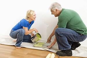 Middle-aged couple pouring paint into tray on drop cloth.