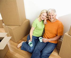 Couple sitting on floor among cardboard moving boxes with coffee