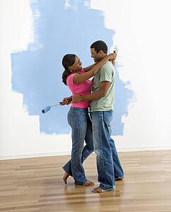 Couple standing together hugging in front of half-painted wall