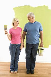 Couple standing in front of half-painted wall with paint supplies 