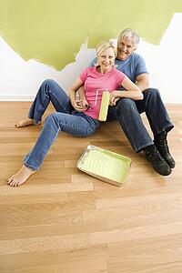 Couple sitting in front of half-painted wall with paint supplies snuggling