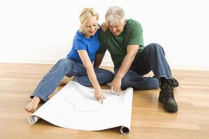 Couple sitting on floor looking at and discussing architectural blueprints together