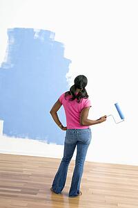 Woman standing next to half-painted wall with paint roller