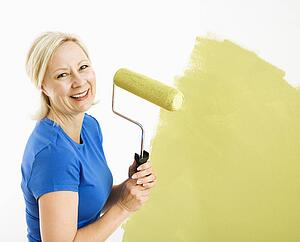 Woman painting wall green with paint roller smiling at viewer