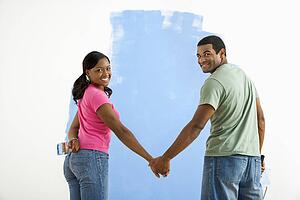 Couple standing together in front of half-painted wall looking at viewer