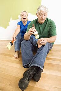 Couple in front of wall they are painting green while male tries to paint women's toenails with paintbrush