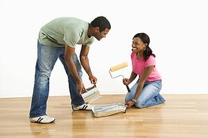 Smiling man pouring paint into tray as female looks on