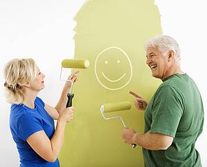 Couple painting wall green, finger-painting smiley face for fun