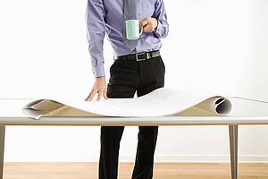Business man standing with coffee cup next to table with blueprints