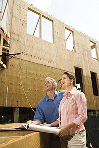Male and female with blueprints observing building construction site