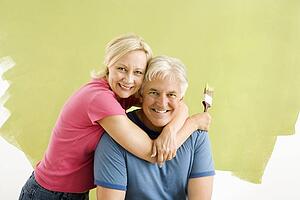 Couple sitting in front of half-painted wall with paintbrushes