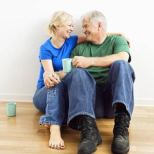 Middle-aged couple sitting on floor snuggling and drinking coffee.