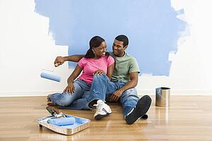 Couple relaxing together next to half-painted wall and painting supplies