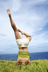 Woman doing headstand in grass near ocean