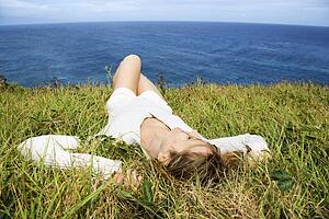 Portrait of young redheaded woman relaxing in grass above the ocean in Maui, Hawaii. 