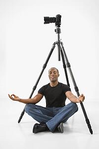 Man sitting meditating under camera and tripod