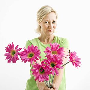 Portrait of smiling adult blonde woman giving bouquet of pink flowers to viewer.