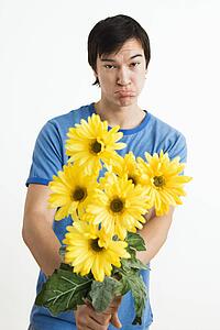 Young man holding bouquet of yellow gerbera daisies with pout on his face.
