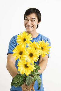 Young man holding bouquet of yellow gerbera daisies smiling.
