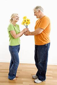 Middle-aged man giving woman bouquet of yellow flowers.