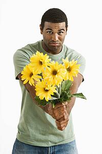 Pouting male holding out bouquet of yellow flowers to unseen person.