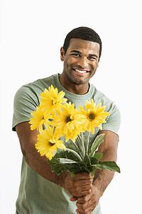Smiling male holding out bouquet of yellow flowers to unseen person.