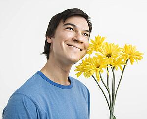 Young man holding bouquet of yellow gerbera daisies smiling.
