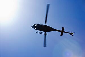 Low angle motion shot of helicopter flying overhead through blue sky