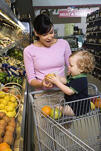 Woman grocery shopping for fruit with toddler