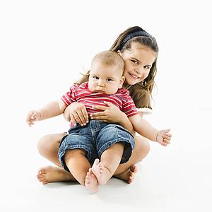 Cute little girl holding baby brother in her lap