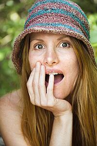 Portrait of pretty redhead with surprised expression on her face wearing hat