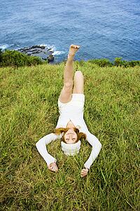 Joyful young woman relaxing in grass near ocean in Maui, Hawaii.