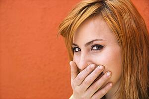 Young redheaded woman laughing with hand over mouth.