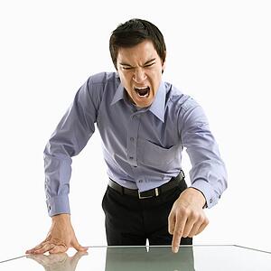 Young Asian business man standing yelling at unseen person.