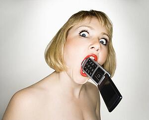 Portrait of young blonde caucasian woman who has a cellphone in her mouth.