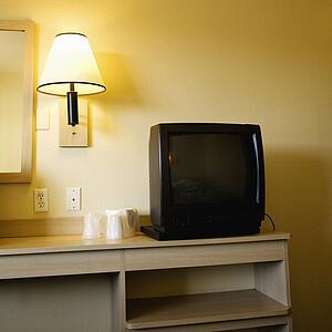 Motel room with TV set on nightstand next to wall lamp