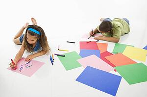 Young boy and girl coloring on construction paper and smiling