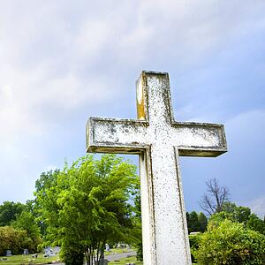 Cross in graveyard against blue sky and clouds.
