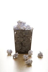 Full wire mesh trash can with crumpled paper scattered around