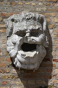 Weathered and broken concrete head hanging from brick wall