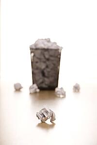 Selective focus of wire mesh trash can with crumpled paper scattered around